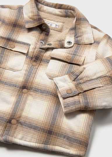 A close-up of a plaid button-up shirt in beige, brown, and muted blue-gray tones, showing the collar, front buttons, chest pockets, and folded sleeve on a light neutral background.
